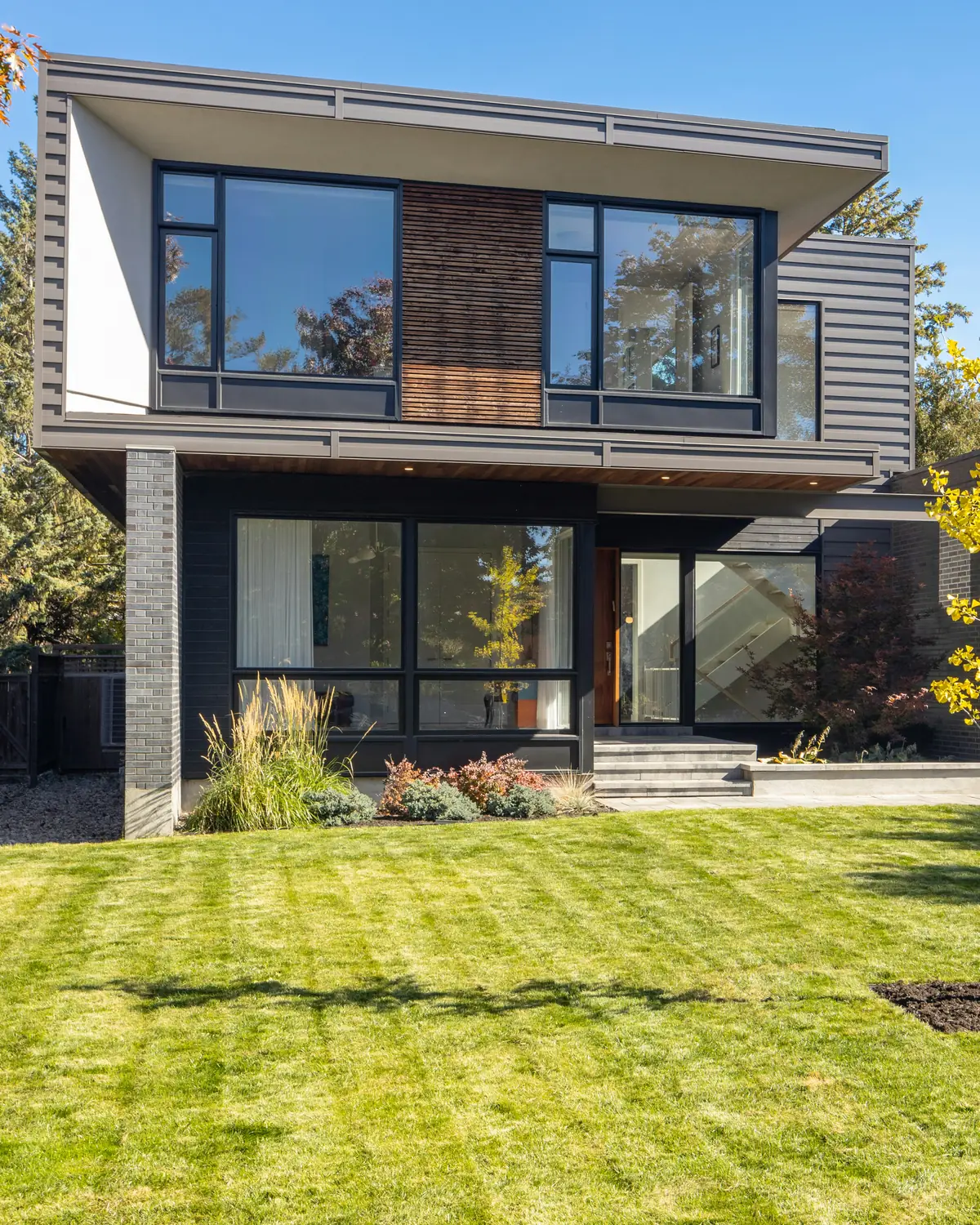 Modern two-story home with dark siding, large windows and a green front lawn